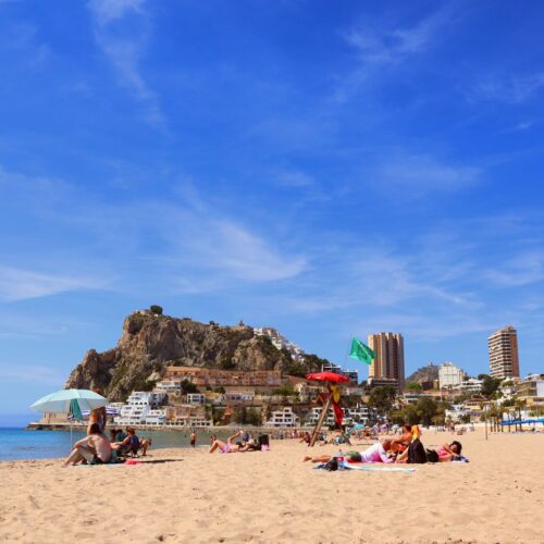 Relaxing beach in Alicante, vibrant day with clear blue skies and bustling city backdrop.