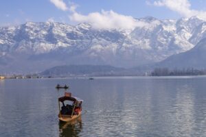 Peaceful view of Dal Lake in Srinagar surrounded by snowcapped Himalayas, featuring traditional boats.
